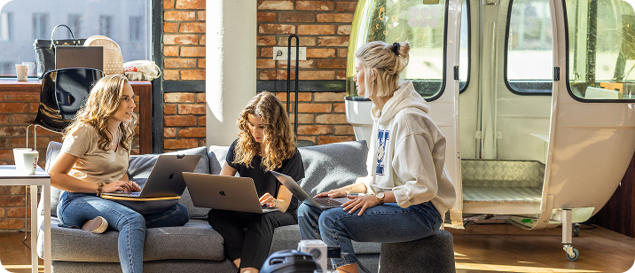 Trzy projektantki i deweloperki z zespołu itCraft siedzące na sofie z laptopami w nowoczesnym biurze z ceglaną ścianą, omawiające architekturę aplikacji medycznej.