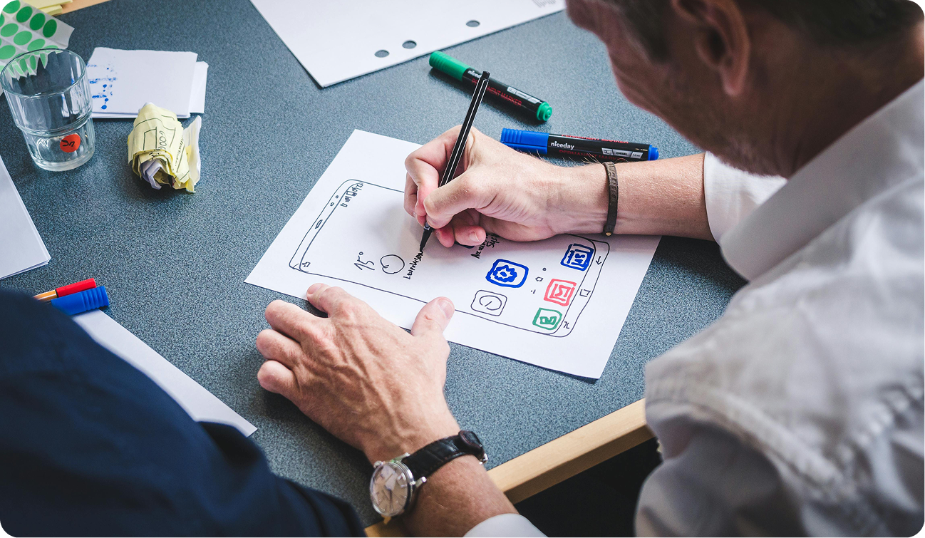 Projektant UX/UI z itCraft rysujący na papierze prototyp i makietę ekranu startowego aplikacji mobilnej dla sektora healthcare.