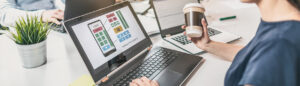 Ekran laptopa z projektem interfejsu aplikacji mobilnej i elementami UI/UX podczas pracy w biurze.