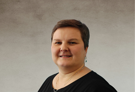 Porträt einer lächelnden Frau mit kurzen dunklen Haaren, bekleidet mit einem schwarzen Oberteil und filigranem Schmuck, in ihrer Funktion als Head of Delivery bei itCraft.