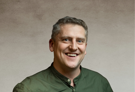Portret uśmiechniętego mężczyzny z krótkimi, lekko przerzedzonymi włosami, ubranego w ciemnozieloną koszulę ze stójką, pełniącego funkcję Head of Sales w itCraft.