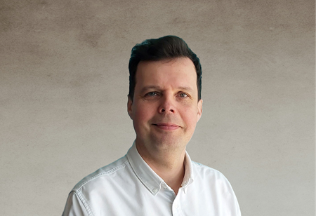 Portret uśmiechniętego mężczyzny z ciemnymi włosami, ubranego w białą koszulę, pełniącego funkcję Senior Project Manager w itCraft.